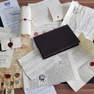 May include: A collection of vintage-style documents and scrolls with wax seals, a brown leather-bound journal, and a black wolf illustration. The documents are on a dark surface with a wooden background.