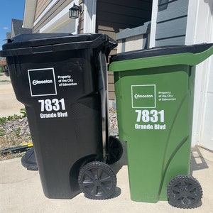 May include: Two large black and green garbage bins with wheels.  Each bin displays 