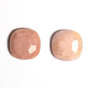 May include: Two pink opal cabochons with a faceted cut. The opals are a light pink color with a white sheen.