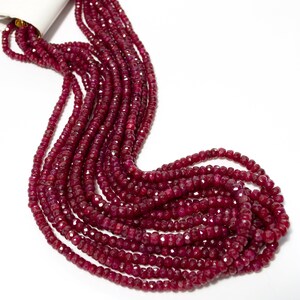 May include: A strand of deep red ruby beads, faceted and polished, arranged in a cascading pattern. The beads are strung on a clear thread and are approximately the same size.