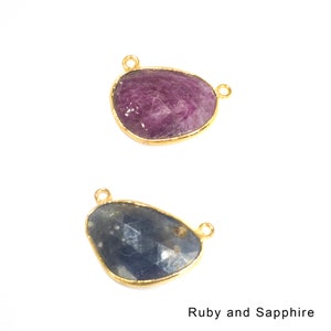 May include: Two gemstone pendants with gold settings. The top pendant is a purple ruby, and the bottom pendant is a blue sapphire.