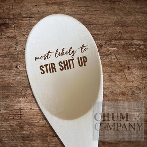 May include: White wooden spoon with the text "most likely to stir shit up" printed in brown on the front.