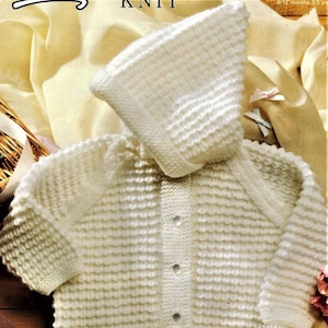 May include: White knitted baby cardigan with a hood and button closure. The cardigan is made with a textured stitch and has a simple design.