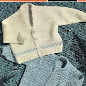 May include: Two knitted baby cardigans, one white with blue trim and the other light blue. Both cardigans have button fastenings and are laid out on a textured blue background. The white cardigan has the text "Model A" and the blue cardigan has the text "Model B".