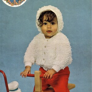 May include: A white knitted baby jacket with a hood, worn by a child riding a red wooden tricycle with a white duck figurine attached.