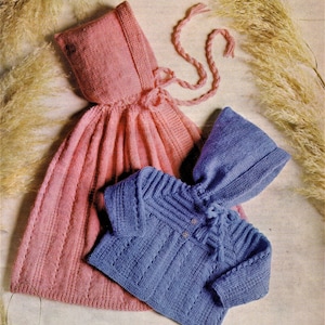 May include: Two knitted baby garments, a pink hooded cape and a blue hooded sweater. Both garments feature a delicate stitch pattern and are tied with matching cords.