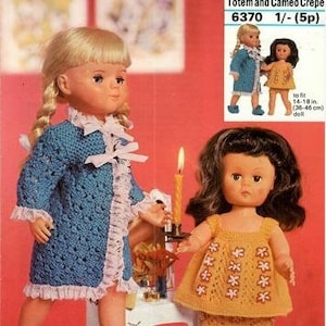 May include: Two dolls wearing crocheted outfits. The doll on the left is wearing a blue and white crocheted robe with a pink trim. The doll on the right is wearing a yellow crocheted dress with a floral pattern. The dolls are both 14-18 inches tall.