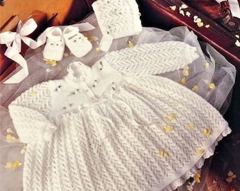May include: A white knitted baby dress with a lace trim and a matching bonnet. The dress has a delicate pattern and is perfect for a special occasion.