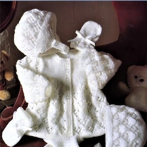 Puede incluir: Un conjunto de ropa de punto blanco para bebé que incluye un cárdigan, un gorro, botines y polainas. El conjunto presenta un delicado patrón de encaje y es perfecto para un recién nacido.