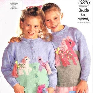 Op de afbeelding: Twee meisjes dragen pastelkleurige truien met een My Little Pony-thema. De truien zijn gebreid en hebben een lichtblauwe, roze en groene kleurstelling. De meisjes houden My Little Pony-speelgoed vast.