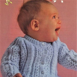 May include: A light blue knitted cardigan with a button closure. The cardigan has a cable knit pattern and is worn by a baby.