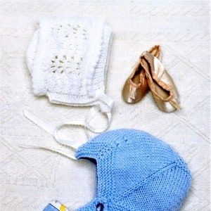 May include: Two knitted baby bonnets, one white with a crocheted design and one light blue. The white bonnet has a white ribbon tied around it. The bonnets are on a white surface.
