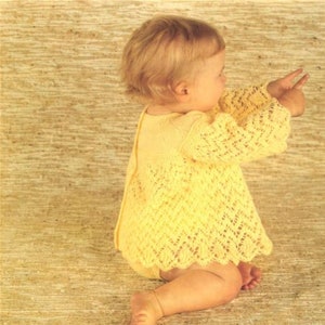 May include: A baby wearing a yellow crocheted dress with a lacy pattern. The dress has a round neckline and long sleeves.