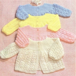 May include: Four knitted baby cardigans in different colours: light blue, yellow, pink, and white. The cardigans are all made with a delicate lace pattern and have a button fastening at the front.