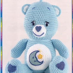 Peut inclure: Un ours en peluche bleu crocheté avec une lune croissante blanche et une étoile jaune sur la poitrine. L'ours a un nez en forme de cœur bleu et des yeux bleus.