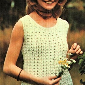 May include: A woman wearing a white crocheted sleeveless top with a delicate openwork pattern. She is holding a bouquet of white daisies in her right hand.