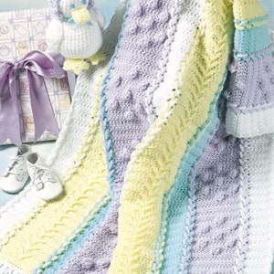 Pode incluir: Um cobertor de bebé em crochê com um padrão listrado em tons de roxo, azul, amarelo e branco. O cobertor tem uma borda de franjas brancas e é feito com um ponto texturizado. Um pequeno brinquedo de pato em crochê está no fundo.