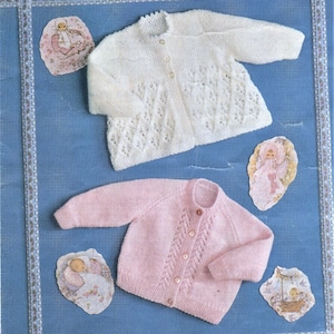 Peut inclure: Deux cardigans en tricot pour bébé, un blanc et un rose, avec un devant boutonné et un motif de dentelle délicat. Les cardigans sont disposés sur un fond bleu.
