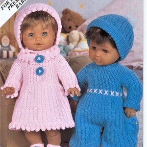 May include: Two knitted doll outfits, one pink and one blue. The pink outfit is a dress with a ruffled collar and the blue outfit is a one-piece jumpsuit with a white embroidered design. Both outfits are for dolls or premature babies.