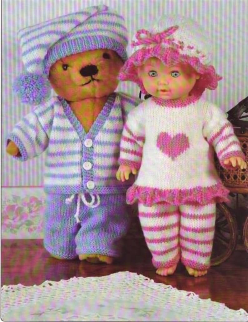 May include: A knitted doll wearing a pink and white striped outfit and a pink and white hat with a bow. The doll is standing next to a knitted teddy bear wearing a blue and white striped outfit and a blue and white hat with a pom-pom.