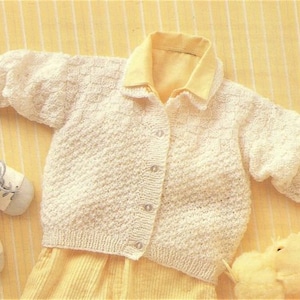 May include: A white knitted cardigan with a button closure. The cardigan has a textured stitch pattern and a collar.