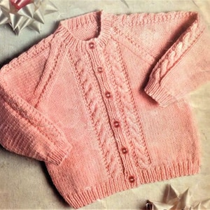 May include: A pink knitted cardigan with a cable knit pattern and button closure.