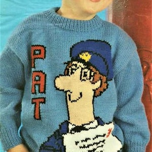 Puede incluir: Un niño pequeño con un suéter de punto azul con una imagen de dibujos animados de un cartero sosteniendo una carta. El suéter tiene la palabra "PAT" tejida en la parte delantera.