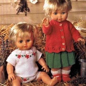 May include: Two dolls wearing knitted outfits. The doll on the left is wearing a white knitted dress with red and green floral embroidery. The doll on the right is wearing a red knitted cardigan with a green skirt.