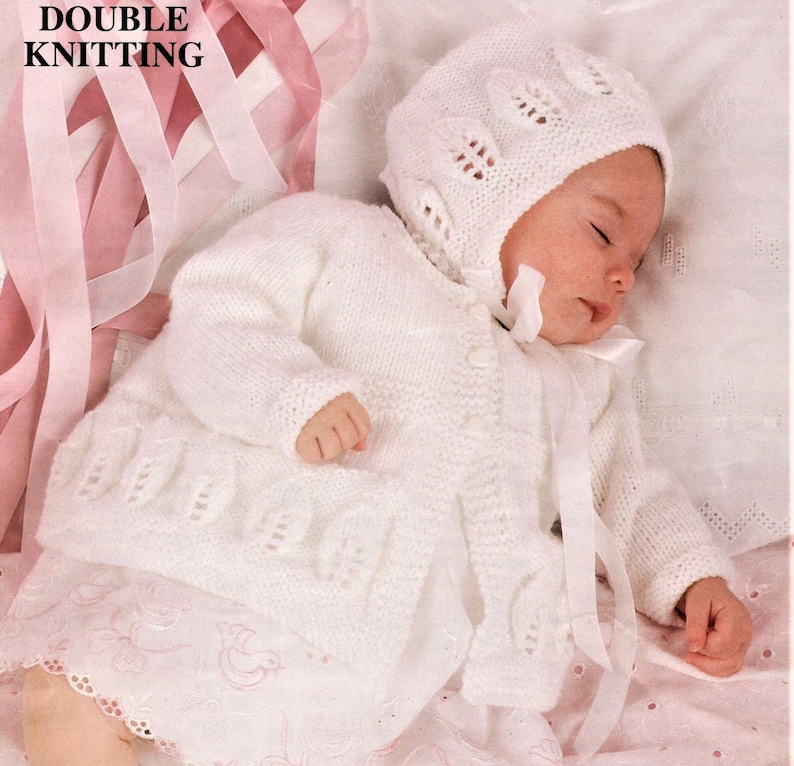 May include: A white knitted baby cardigan and matching bonnet with a delicate lace pattern. The set is made with a soft yarn and features a button closure on the cardigan.