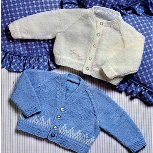 May include: Two knitted baby cardigans, one white with pink buttons and one blue with white trim.