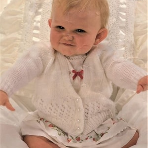 May include: A white knitted baby cardigan with pearl buttons and a red bow. The cardigan is 18-20 inches in size and is made for babies.