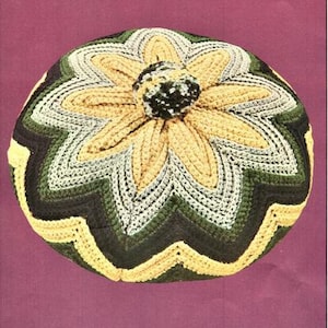 May include: A crocheted hat with a flower design in shades of yellow, green, and brown. The hat has a textured, bumpy surface.