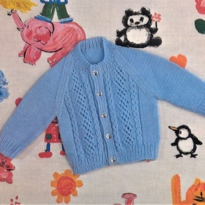 May include: A light blue knitted baby cardigan with a button-up front and a cable knit pattern.