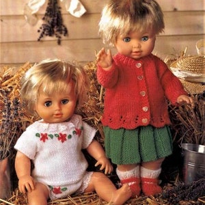 Puede incluir: Dos muñecas con atuendos tejidos. La muñeca de la izquierda lleva una blusa tejida blanca con flores rojas y una parte inferior tejida blanca. La muñeca de la derecha lleva una chaqueta tejida roja con una falda tejida verde. Ambas muñecas tienen el pelo rubio y los ojos azules.