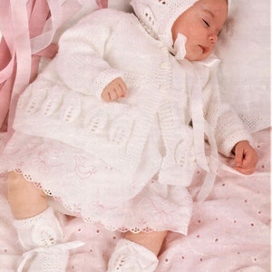 以下が含まれることがあります： レースのトリムが付いた白いニットのベビー服と帽子、ブーティのセット。繊細な透かし模様が施されており、特別な機会に最適です。