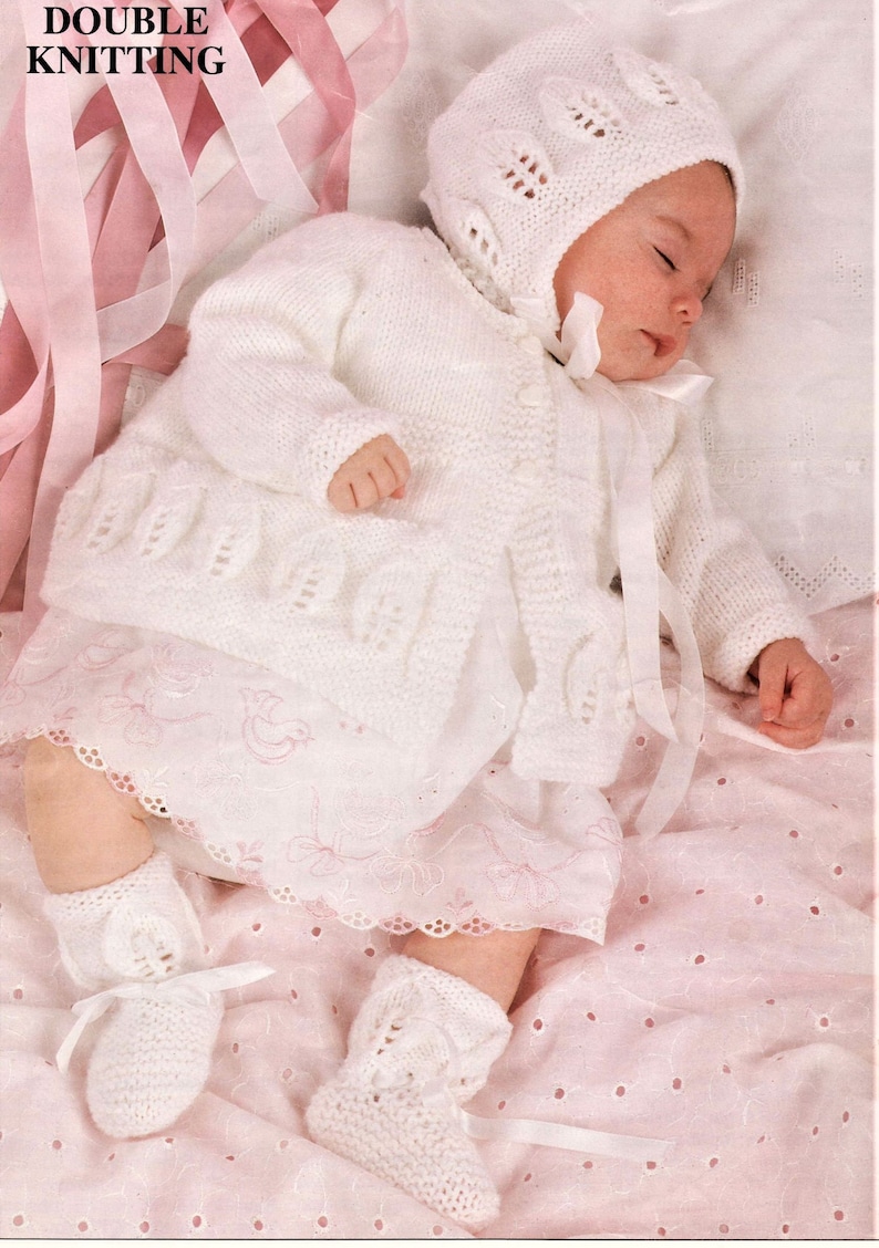 May include: A white knitted baby outfit with a matching hat, booties, and a lace trim. The outfit features a delicate openwork pattern and is perfect for a special occasion.