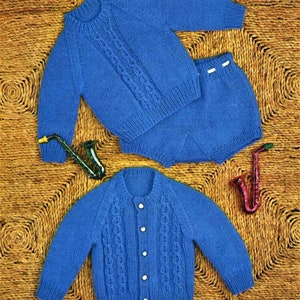 May include: A blue knitted sweater and matching shorts set for a baby. The sweater has a cable knit pattern and a round neckline. The shorts have a button closure.
