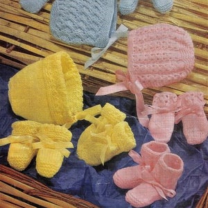 May include: Hand-knitted baby sets in pastel shades of blue, yellow, and pink, comprising booties, bonnets, and mittens. Each piece is finished with satin ribbons. The items are arranged in a woven basket.