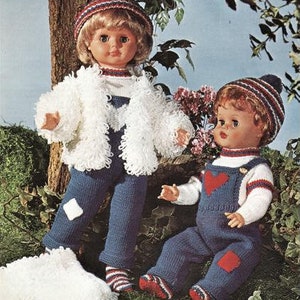 Puede incluir: Dos muñecas con atuendos tejidos. La muñeca de la izquierda lleva una chaqueta blanca peluda, pantalones vaqueros azules y un gorro rojo, blanco y azul. La muñeca de la derecha lleva un mono tejido azul con un corazón rojo, un suéter blanco con rayas rojas y azules y un gorro rojo, blanco y azul.