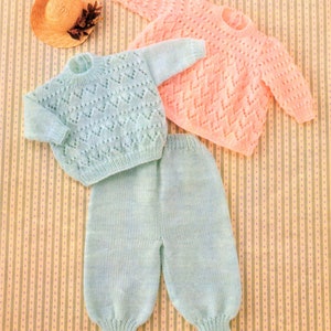 May include: A knitted baby outfit in light blue and pink. The set includes a sweater, pants, and a hat. The sweater has a delicate lace pattern. Sizes 16-22 in, 41-56 cm.