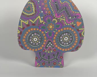 May include: A decorative skull-shaped object with a gray base, adorned with colorful patterns. The design includes orange, purple, yellow, and blue dots and shapes, with a lightning bolt and flower motif. The eyes are represented by two circles with white dots.