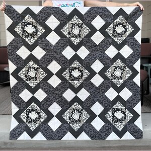 May include: Black and white quilt with a diamond pattern and floral designs. The quilt is made of fabric with a subtle texture.