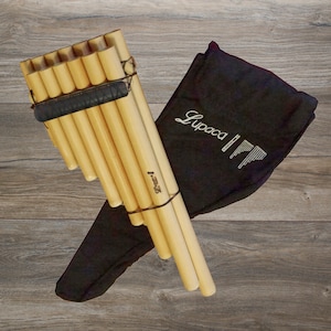 Puede incluir: Un conjunto de flautas de pan de madera con una funda de transporte negra. Las flautas de pan están hechas de bambú natural y tienen una correa de cuero marrón. La funda tiene la palabra "Lupaca" bordada.