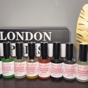 May include: A collection of perfume oil bottles with black caps and labels. The labels feature the text "Malar Aromas" and various scent names like "Pistachio Gelato" and "Oud Satin Mood." The word "LONDON" is visible in the background.