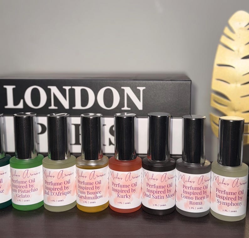 May include: A collection of perfume oil bottles with black caps and labels. The labels feature the text "Malar Aromas" and various scent names like "Pistachio Gelato" and "Oud Satin Mood." The word "LONDON" is visible in the background.