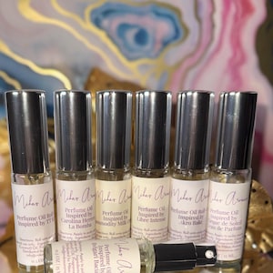 Pode incluir: S&atilde;o exibidos seis frascos de &oacute;leo de perfume roll-on com tampas prateadas. Cada frasco tem um r&oacute;tulo com texto, incluindo "&Oacute;leo de Perfume" e v&aacute;rios nomes de fragr&acirc;ncias como "Carolina Herrera". Os frascos est&atilde;o em uma superf&iacute;cie reflexiva.