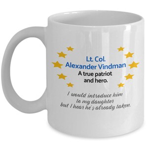 May include: White ceramic coffee mug with a blue and yellow design. The mug features a quote about Lt. Col. Alexander Vindman, a true patriot and hero. The quote reads, "I would introduce him to my daughter but I hear he's already taken."