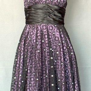 May include: A formal halter dress in shades of purple and black. The bodice features a V-neck and a ruched black satin band at the waist. The skirt is a full A-line, with a floral lace overlay and sparkling accents. The dress is displayed on a mannequin.