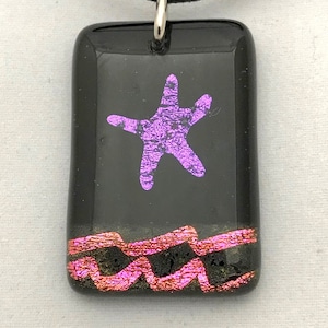 May include: A black glass pendant with a pink starfish design and a red and gold iridescent border. The pendant is on a black cord.