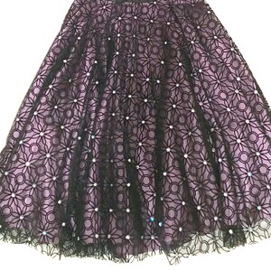 May include: A black lace skirt with a floral pattern and a lavender lining. The skirt is embellished with small, sparkling accents. The skirt has a flared silhouette, suitable for formal occasions.